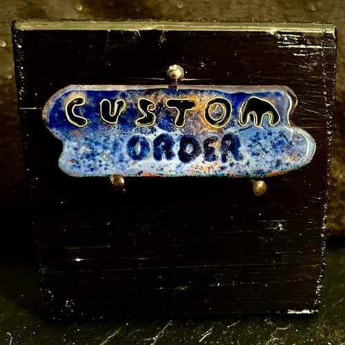 Cloisonné enamel piece reading 'Custom Order' in deep blue on a black pine display stand — handcrafted by A. Fraction, Vilnius, example of a custom enamel commission