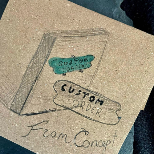 Pencil sketch of a custom enamel commission concept drawn on kraft paper, photographed on slate — showing the design stage of a bespoke miniature enamel order by A. Fraction, Vilnius