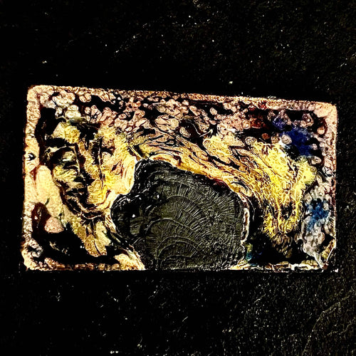 Fly Nest – original enamel miniature on copper,  up close view of the rectangular piece resting on dark slate. Swirling yellow, amber and black kiln-fired enamel around a burned grey central form. Handcrafted enamel art by A. Fraction.