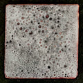 Whale Skin – original experimental vitreous enamel miniature on copper, front view on dark slate. Grey-white enamel with dense bubbled, pitted texture and copper-red edges, not  resembling actual whale hide. Handcrafted enamel art by A. Fraction.