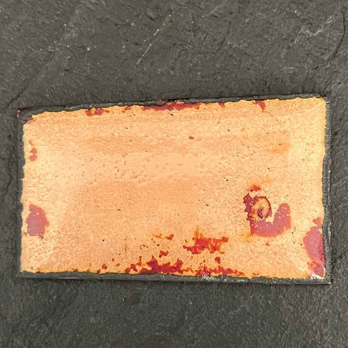 Fly Nest – reverse side of the original enamel miniature on copper, showing the raw copper back with warm gold and red kiln-fired firing marks, resting on dark slate. Handcrafted enamel art by A. Fraction.