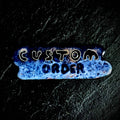 Small vitreous enamel piece on copper reading "Custom Order" in hand-drawn lettering, blue textured surface with fine silver wire cloisonné outlines, by A. Fraction