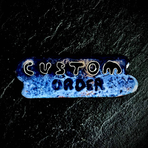 Small vitreous enamel piece on copper reading "Custom Order" in hand-drawn lettering, blue textured surface with fine silver wire cloisonné outlines, by A. Fraction