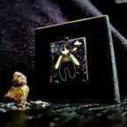 The Wild Within, House Zoo — The Wild We Live With. Displayed on its handmade black wood stand, styled with a small stone figure in the foreground. Moody dark atmosphere. A. Fraction.