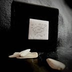Cloud enamel miniature mounted on handmade matte black pine stand against a dark textured surface, with white seed pods in the foreground, by A. Fraction