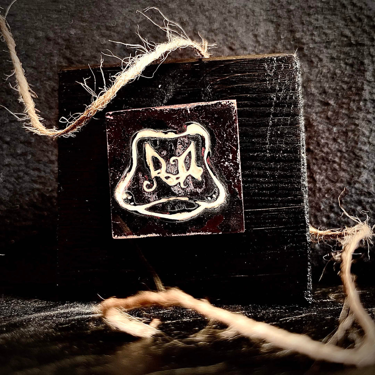 Cow's Hairy Nose champlevé enamel miniature mounted on handmade matte black pine stand, styled with natural rope on a dark textured surface, by A. Fraction
